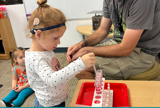female child wearing a cochlear implant playing with a science toy